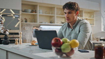 Handsome freelancer working laptop sitting kitchen close up. Man drinking coffee