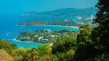 Viewpoint of Karon Beach, Kata Beach and Kata Noi in Phuket, Thailand. The beautiful coastal basin and surrounding buildings are visible from a distance and the sky is blue from a high vantage point.