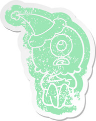 quirky cartoon distressed sticker of a cyclops alien spaceman wearing santa hat