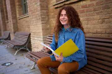Portrait of young happy Caucasian red head student outside the university building looking at the...