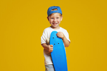 Charming blonde boy holding blue longboard and smiling while looking at camera. Isolated over...