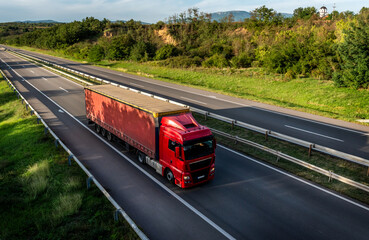Highway scene with Red lorry truck with red trailer passing on a highway driving at beautiful...
