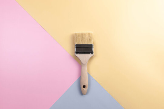 Top view of paint brush on colourful background. Blue, pink and yellow background. Colourful wallpaper, flat lay, copy space.