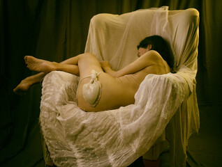 woman without clothes lying in an armchair on lace and tulle in a romantic attitude V