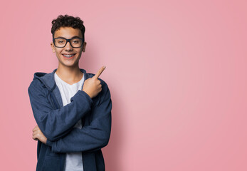 Excited happy black curly haired man in braces brackets, wear glasses, zipup hoodie jaket advertise show point sales slogan text area, isolated rose pink background. Dental care, ophthalmology ad.