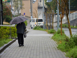 雨の日の住宅地で歩く一人のシニア女性の姿