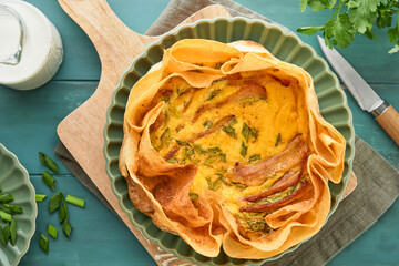 Homemade quiche or tart with slices of bacon and leeks with tortilla instead of dough on wooden...