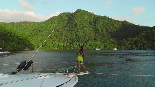 A youthful girl in beach attire is seen on a yacht from an aerial drone perspective in the Caribbean.
