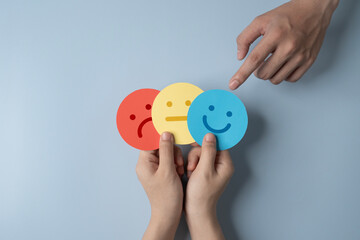 paper cut smiley face, stressed and sad in hands on light blue background. positive thinking,...