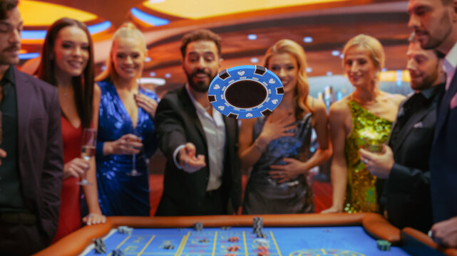 Casino Players Making Bets at a Roulette Table. Vibrant Crowd of International People Enjoying Nightlife in City. Male Gambler Tossing a Casino Chip with a Template Placeholder Flying At the Camera