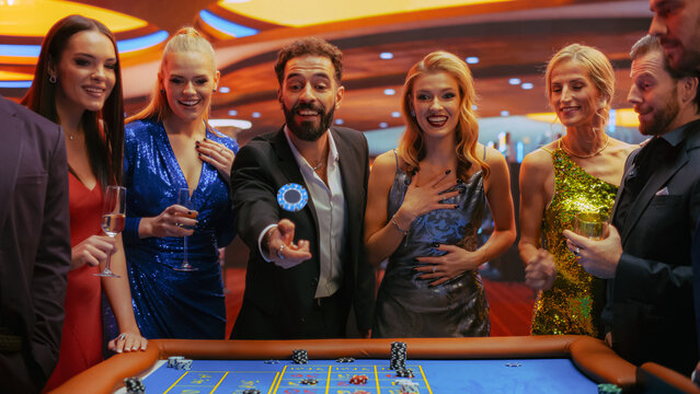 Casino Players Making Bets at a Roulette Table. Vibrant Crowd of International People Enjoying Nightlife in a City. Male Gambler Tossing a Casino Chip with a Template Placeholder Flying At Camera