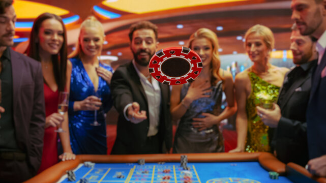 Multiethnic Young Adults Playing an Engaging Game of Roulette, Spending a Fun Evening in a Luxurious Hotel Casino. Enthusiastic Gambler Tossing a Red Casino Chip with a Template Placeholder