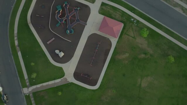 Spinning and ascending aerial view of swings, slides, and other playground equipment at a city park on a summer morning.