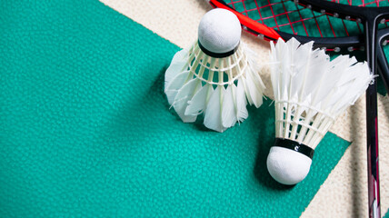 Fototapeta na wymiar White badminton shuttlecocks and badminton rackets on green floor indoor badminton court soft and selective focus on shuttlecocks and the rackets