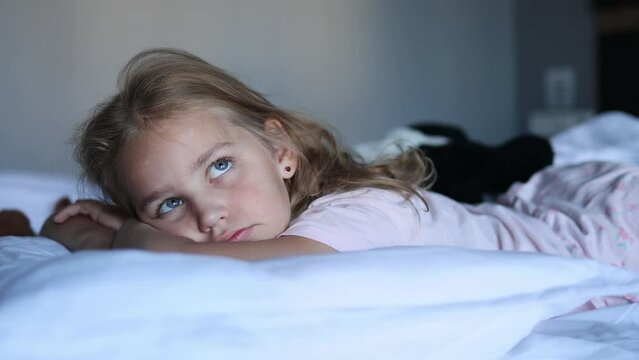 A little blonde girl lies in her cozy bed on her stomach under a warm and cozy blanket. The concept of rest, relaxation and awakening.