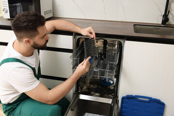 Serviceman examining dishwasher cutlery rack in kitchen