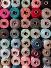 A display of soft pastel colored sewing threads, aligned in rows for a soothing visual, suitable for craft stores.