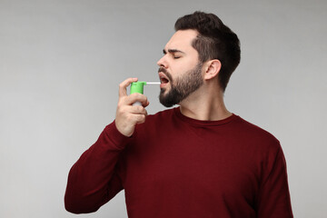 Young man using throat spray on grey background