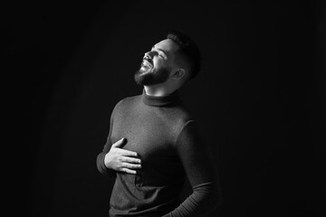 Portrait of handsome bearded man laughing on dark background, toned in black and white