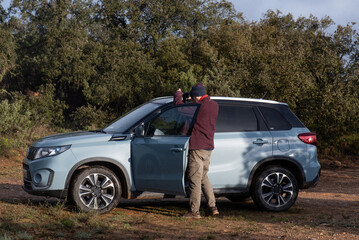 man taking out his binoculars to get into the 4x4 car, walking in the mountains and looking for animals, naturalist in mountain clothing © Cristina