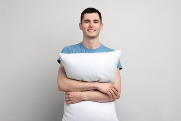 Happy man in pyjama holding pillow on light grey background