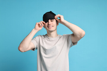 Naklejka premium Happy man in pyjama and sleep mask on light blue background