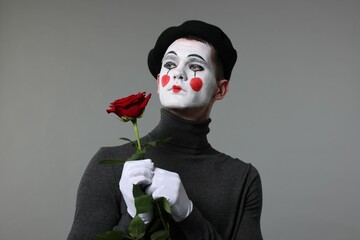 Portrait of mime artist with red rose on grey background