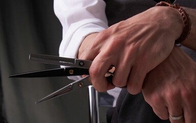 Closeup of an elegant tailor wearing a suit sitting holdng scissors