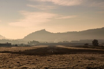Airport runway with direction signs surrounded by grassy ground and hills with trees at sunset