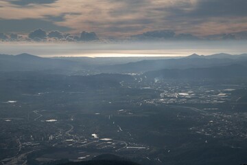 Aerial shot of the clouds and high rocky mountains covered with a city