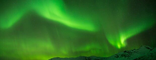 Panoramic shot of bright green aurora northern lights over mountains in Norway