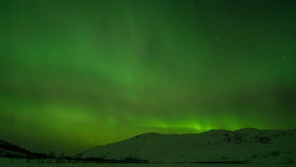 Beautiful shot of bright green aurora northern lights over mountains in Norway