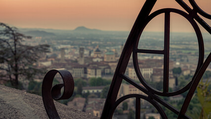 Selective focus shot of a metal fence with the Bergamo cityscape in the background