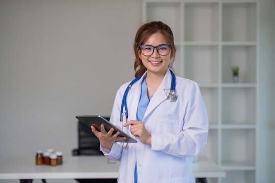 Confident Asian female doctor Standing and checking patient information on a tablet in the clinic.