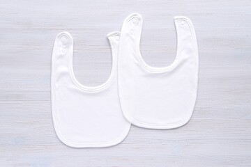 Two white blank cotton baby bibs, mockup for design presentation, minimal style flat lay.