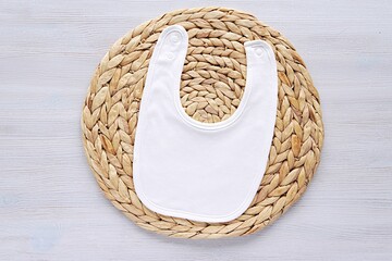 White cotton baby bib mockup for design presentation, baby announcement, flat lay on wicker mat.