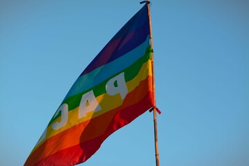 Closeup of a LGBTQIA flag against a cloudless blue sky at sunset