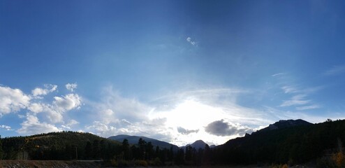 Panoramic shot of the sunlight behind the clouds over the fir forest trees and mountains