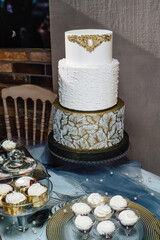 Gilded wedding cake with gilded decorations, white and beautiful against a loft wall.