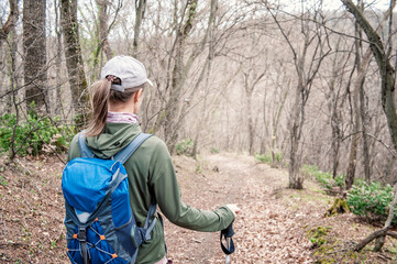 Woman tourist with backpack and walking stick hiking the forest path