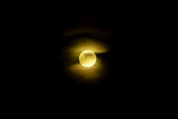 beautiful yellow full moon covered with clouds on the black night sky