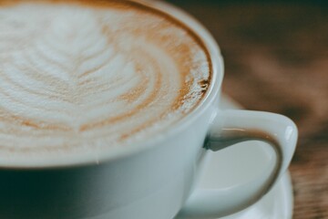 Aesthetic closeup of latte art in a white coffee mug on a blurred wooden surface