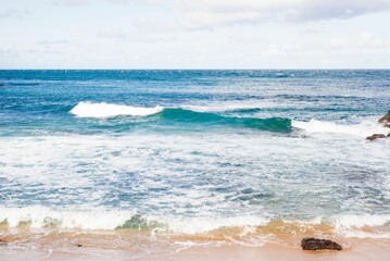 Scenic shot of foamy ocean waves crashing on the sand of a coast on a sunny day