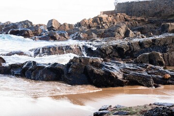Closeup shot of a large rock on the coast of an ocean with foamy waves crashing on it