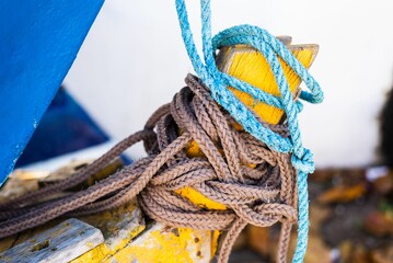 Closeup shot of a brown and blue rope knots on the tip of a yellow boat