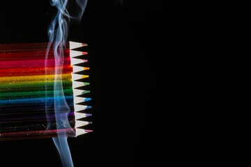 Closeup of colored pencils grouped on black background with white smoke coming from below