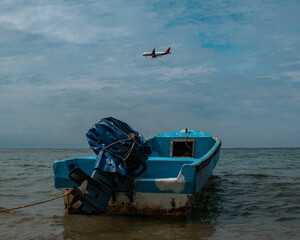Closeup shot of old blue boat floating in sea with plane flying in sky