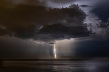 Lightning in a stormy night sky over a seascape hiding behind the clouds