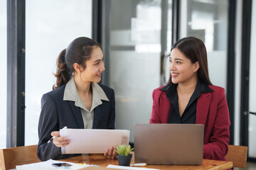 Fototapeta premium Two asian businesswomen in suits are sitting at a table with a laptop and a piece of paper