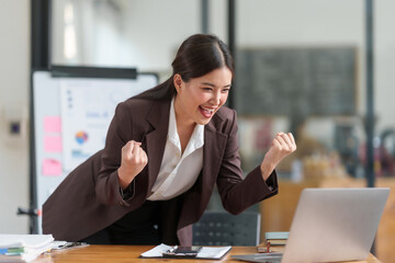 Joyful female professional exuberantly celebrating a victory or success while working at her office desk.